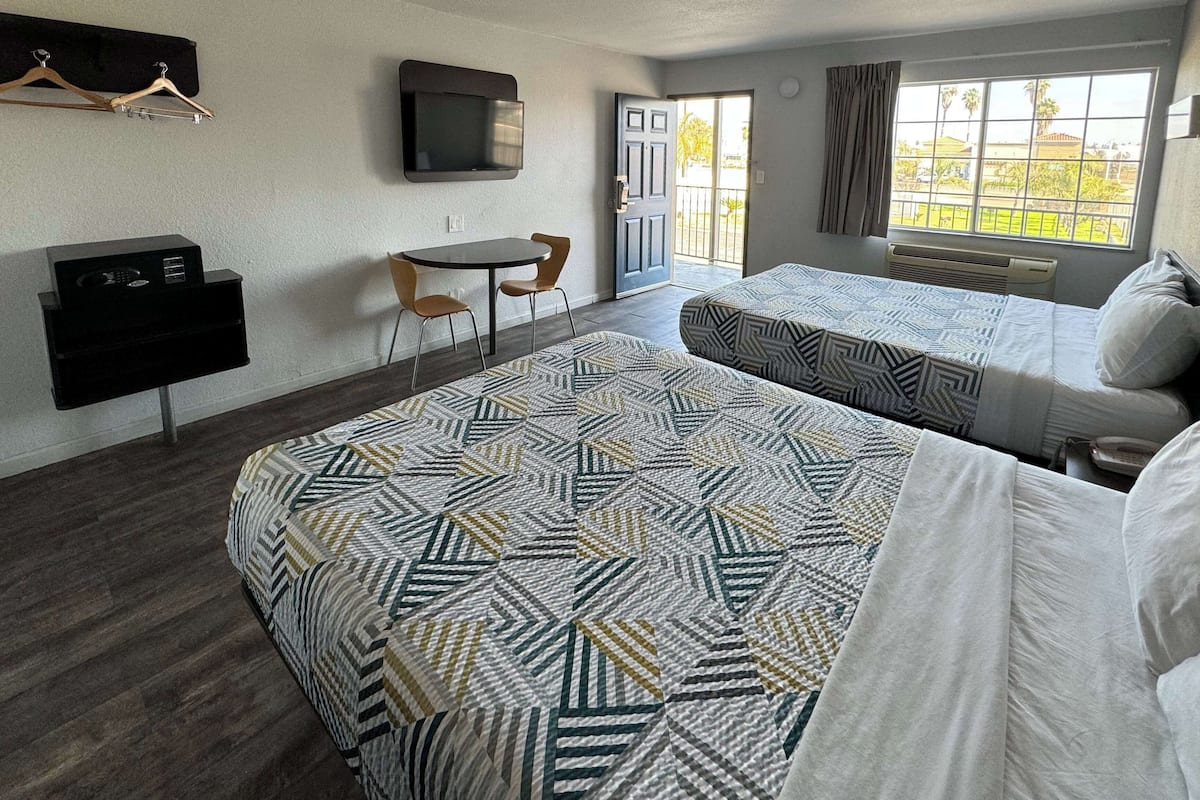 Une chambre d’hôtel avec deux lits, un bureau, une chaise, une télévision et une fenêtre donnant sur des palmiers.