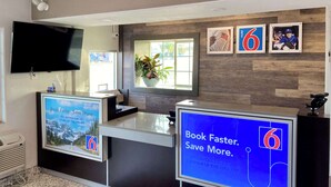 Un comptoir d’accueil moderne doté de deux écrans diffusant du contenu promotionnel, d’un téléviseur à écran plat placé au-dessus, et d’un mur en bois orné de tableaux encadrés.