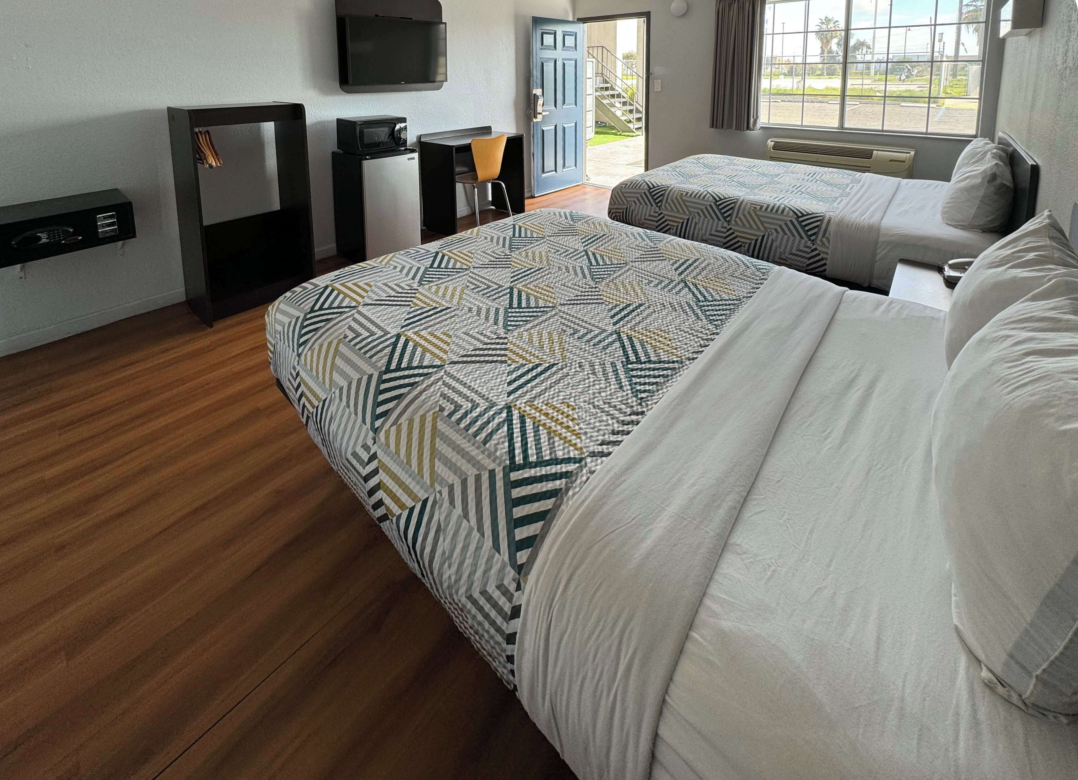 Ein Hotelzimmer mit einem großen Bett, einem Schreibtisch mit Stuhl, einem Fernseher, einer kleinen Kühlbox und einem Fenster mit Blick nach draußen.