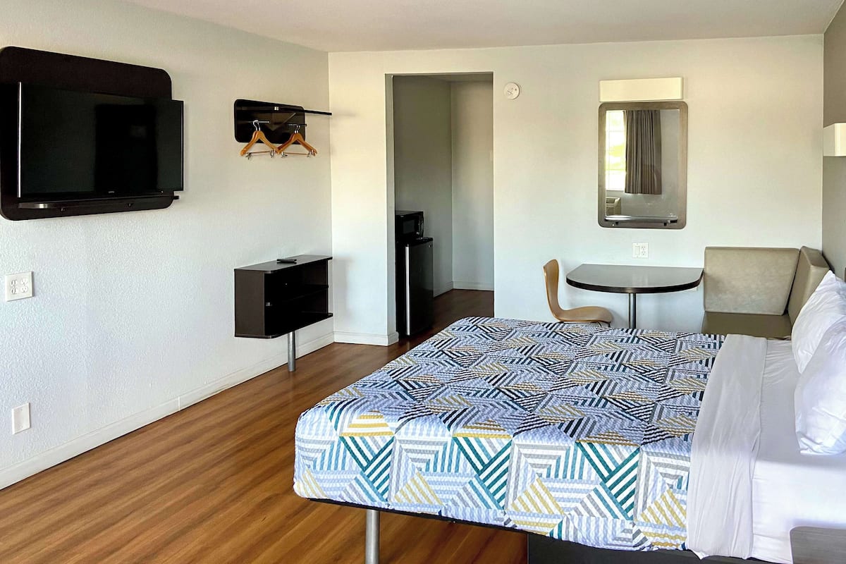 Une chambre d’hôtel équipée d’un lit, d’un bureau, d’une chaise, d’une télévision et d’un miroir.