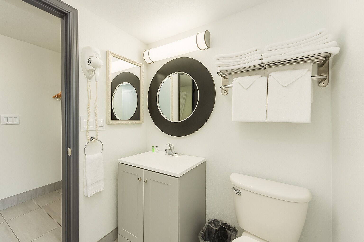 A bathroom with a toilet, sink, two mirrors, a towel rack, and a hairdryer.