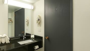 Un baño con un lavamanos negro, un espejo, un perchero y una puerta.