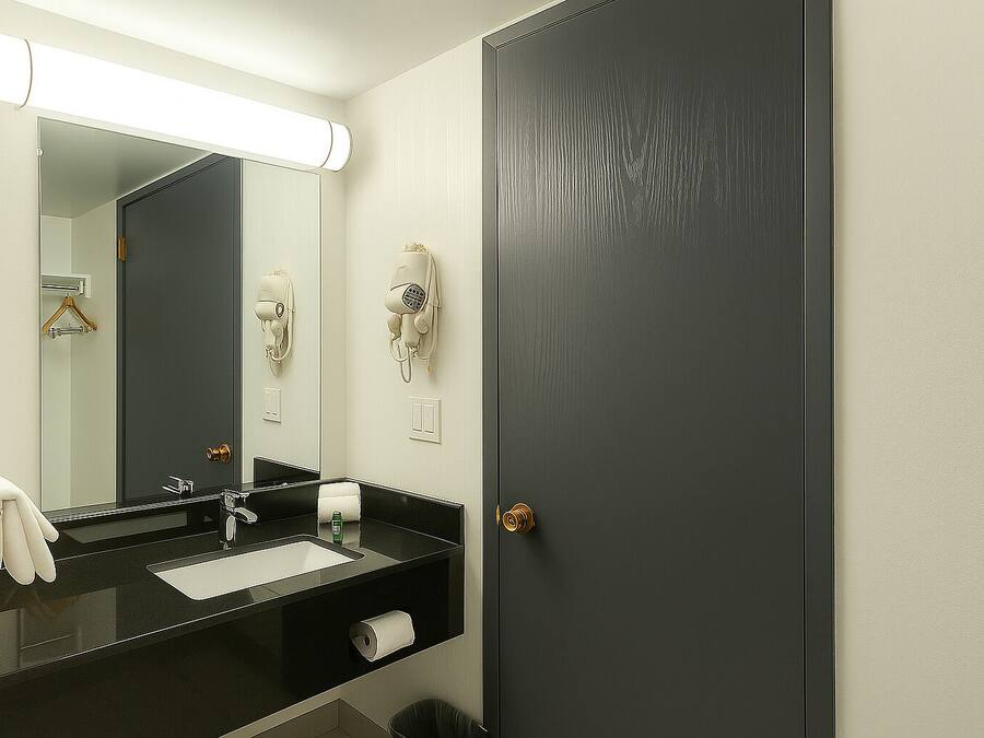 Un baño con un lavamanos negro, un espejo, un perchero y una puerta.