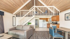 Un espacio habitable tipo loft con techo alto, una escalera que conduce a un nivel superior, una zona de cocina y un área de estar con sofá y sillones.