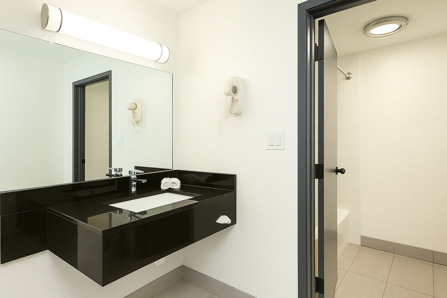 A modern bathroom with a black sink, a mirror, a towel rack, and a shower area.