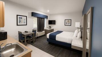 A hotel room with a bed, a desk, a chair, a TV, and a sink.