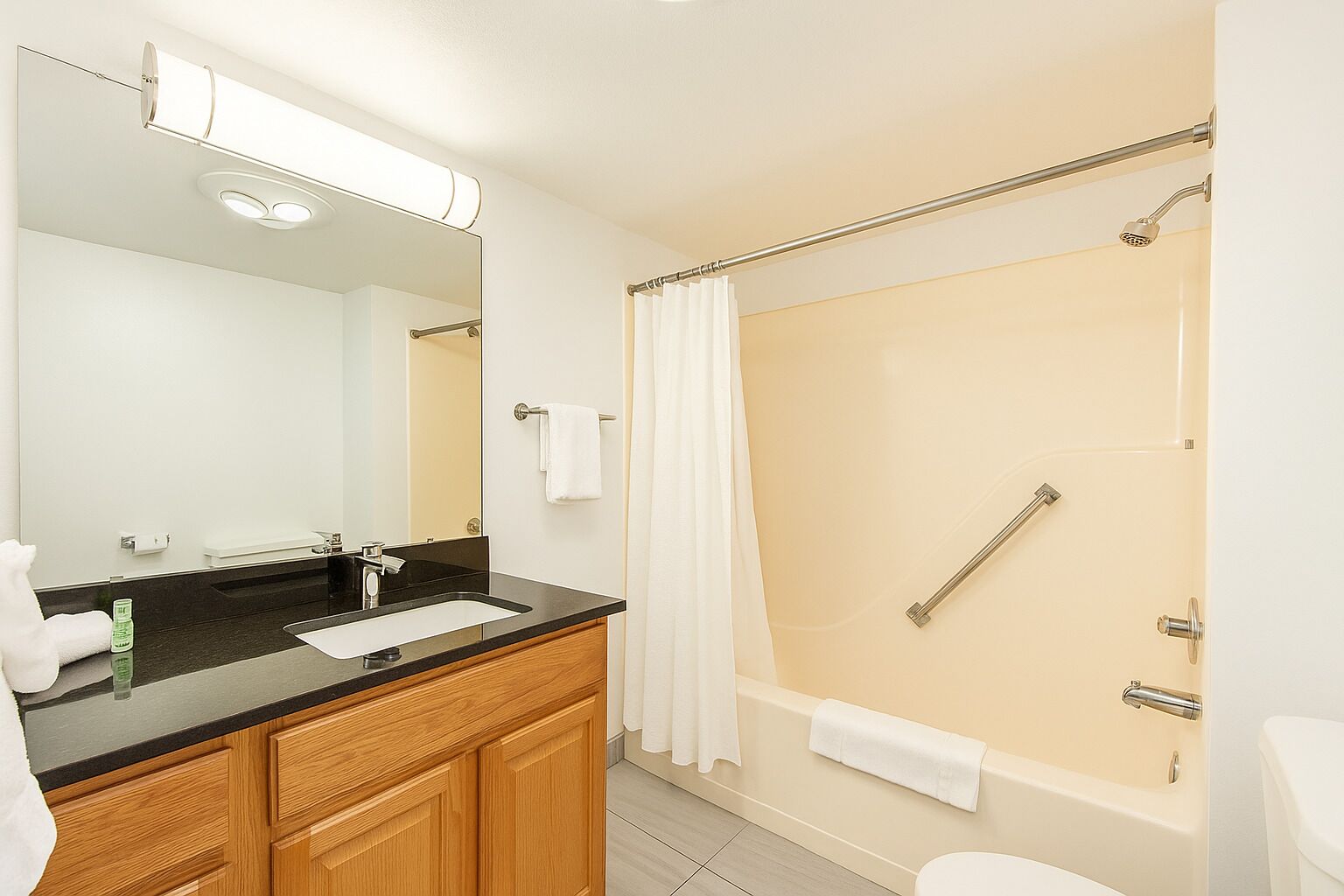 Un baño con un lavamanos negro, armarios de madera, un espejo, ducha con puerta de vidrio y un inodoro.