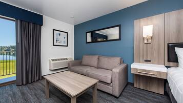 Habitación de hotel con sofá, una mesita, cama, espejo y ventana con vista a un lago.