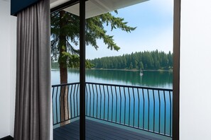 A balcony with a view of a lake, trees, and a sailboat. - Oyster Bay Inn & Suites (Bremerton)