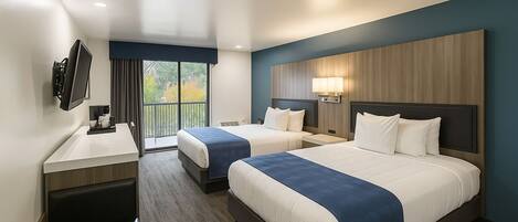 A hotel room with two beds, a desk, a TV, and a balcony.