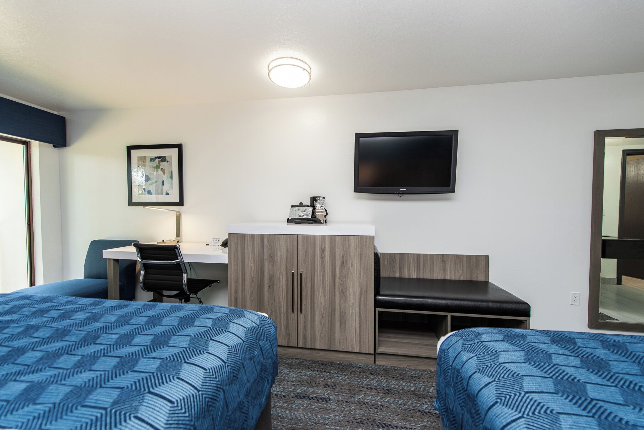 A hotel room with two beds, a desk, a chair, a television, and a framed picture on the wall.