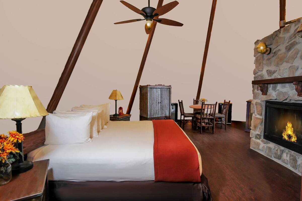 A room with a bed, a fireplace, a dining table with chairs, and a ceiling fan.