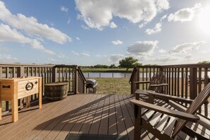 A wooden deck with a grill, chairs, and a wooden table.