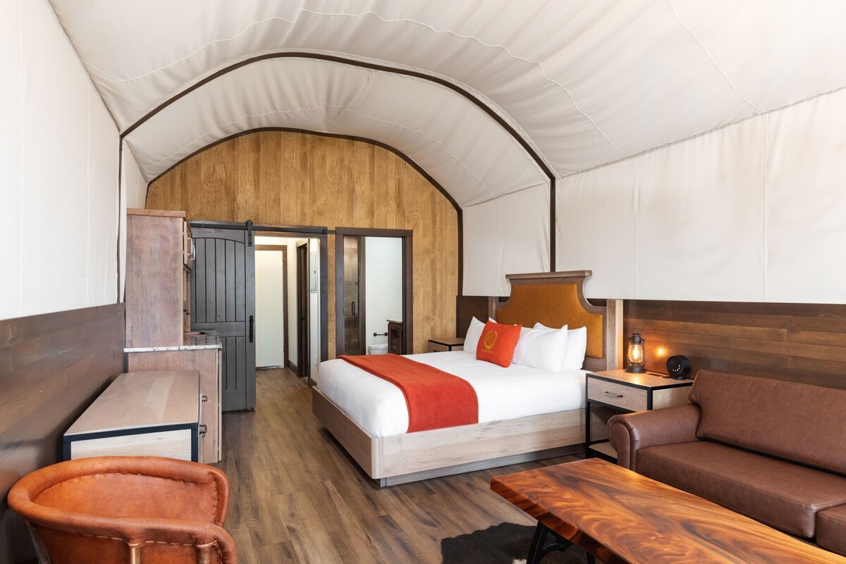 A room with a bed, a desk, a chair, a sofa, and a lamp.