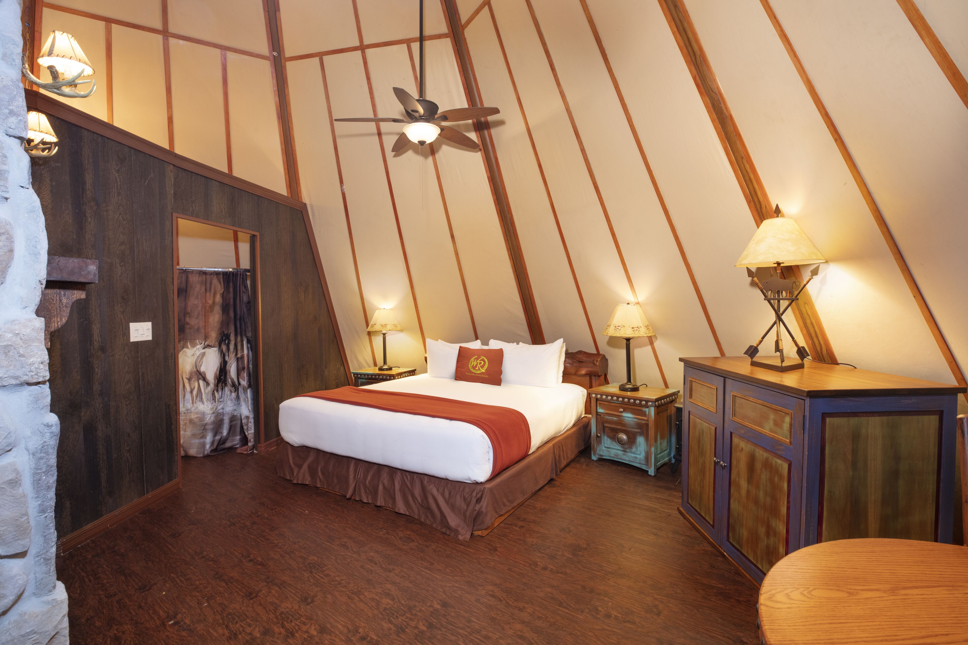 Een slaapkamer met een schuine kap, een bed met witte beddengoed en een bruine accentkleur, twee nachtkastjes met lampen, en een houten kast.