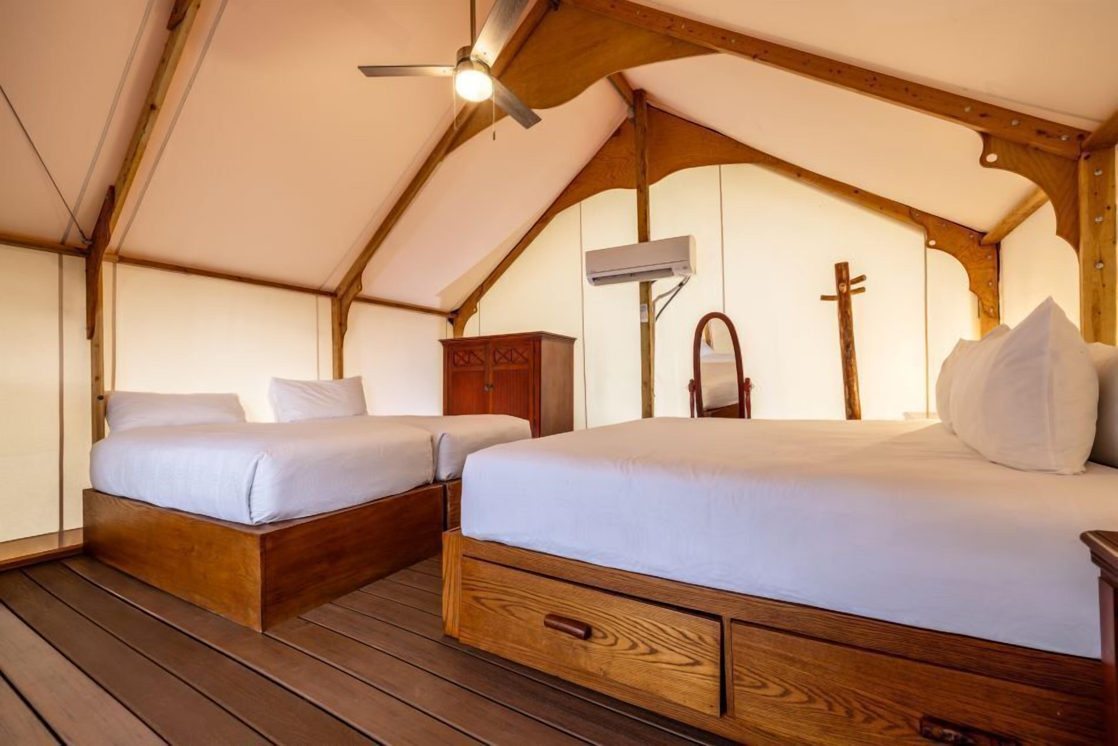 A tent-style room with two wooden beds, a ceiling fan, and a wooden cabinet.