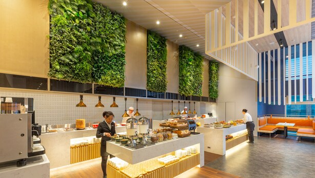 Een modern café met een centraal aanrecht, een zitgedeelte met oranje kussens en groene wanden.
