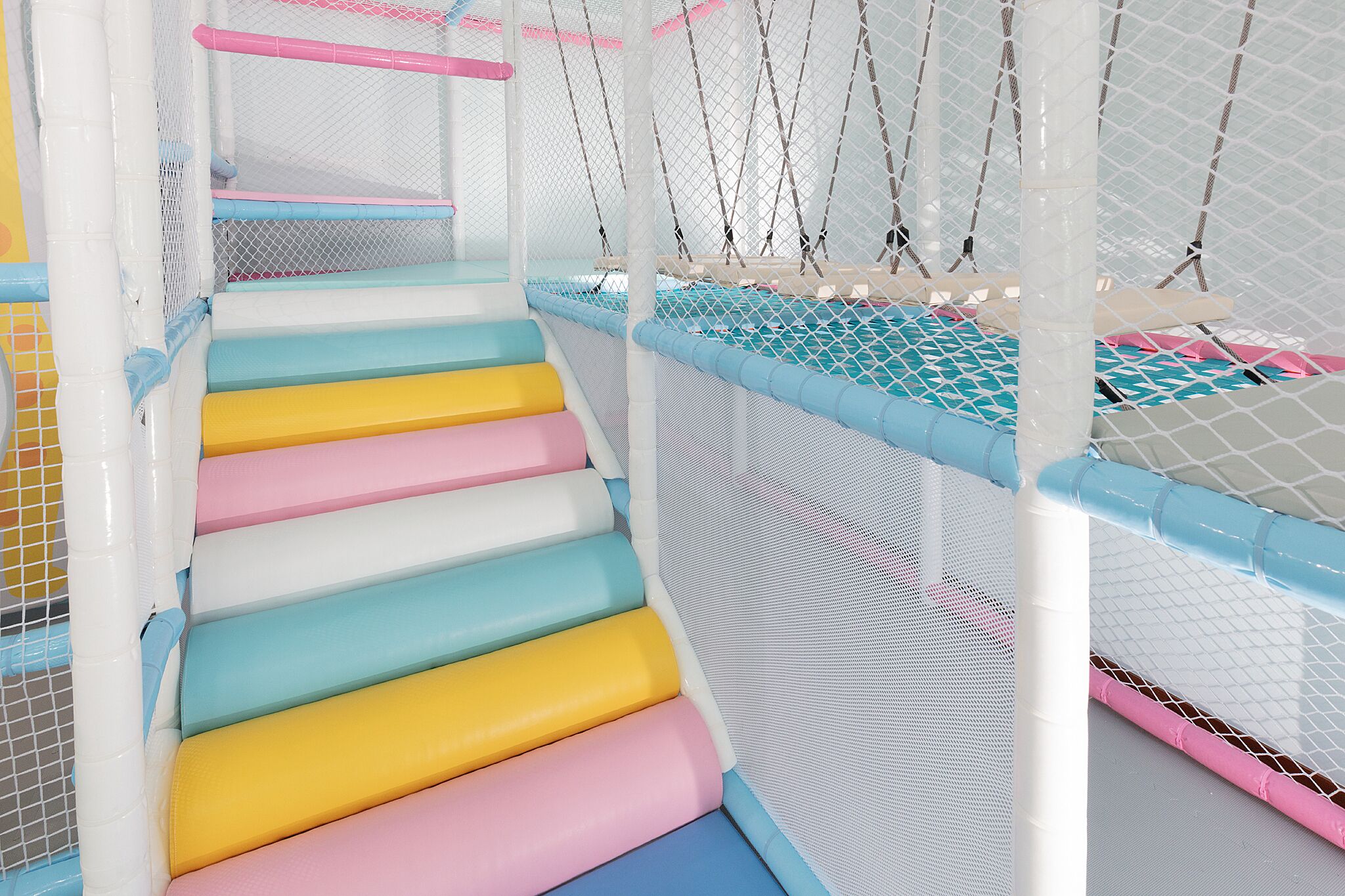 A multi-level indoor play area with colorful steps and netted walls.