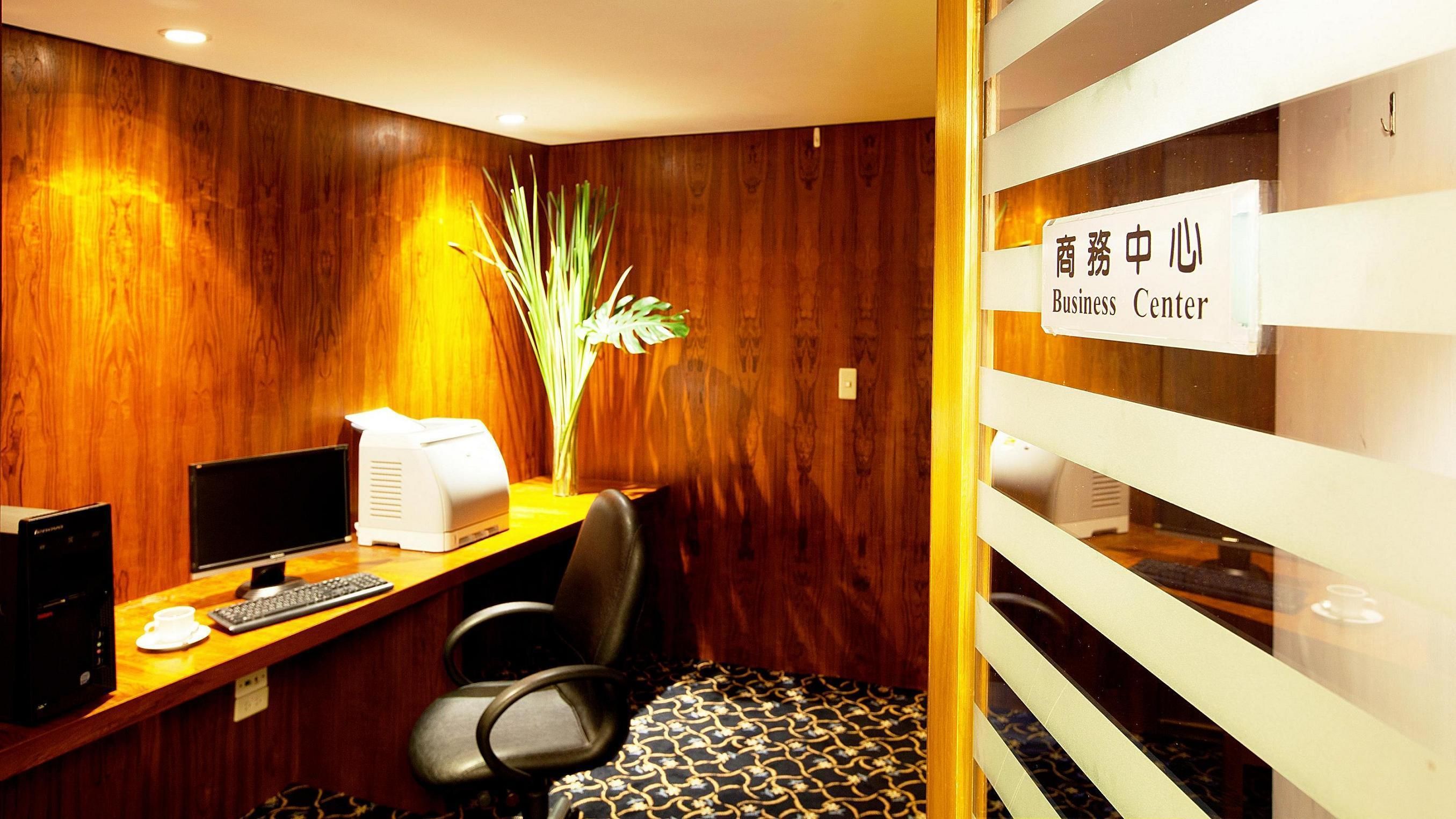 A business center with a wooden wall, a desk with a computer, a printer, and a chair.
