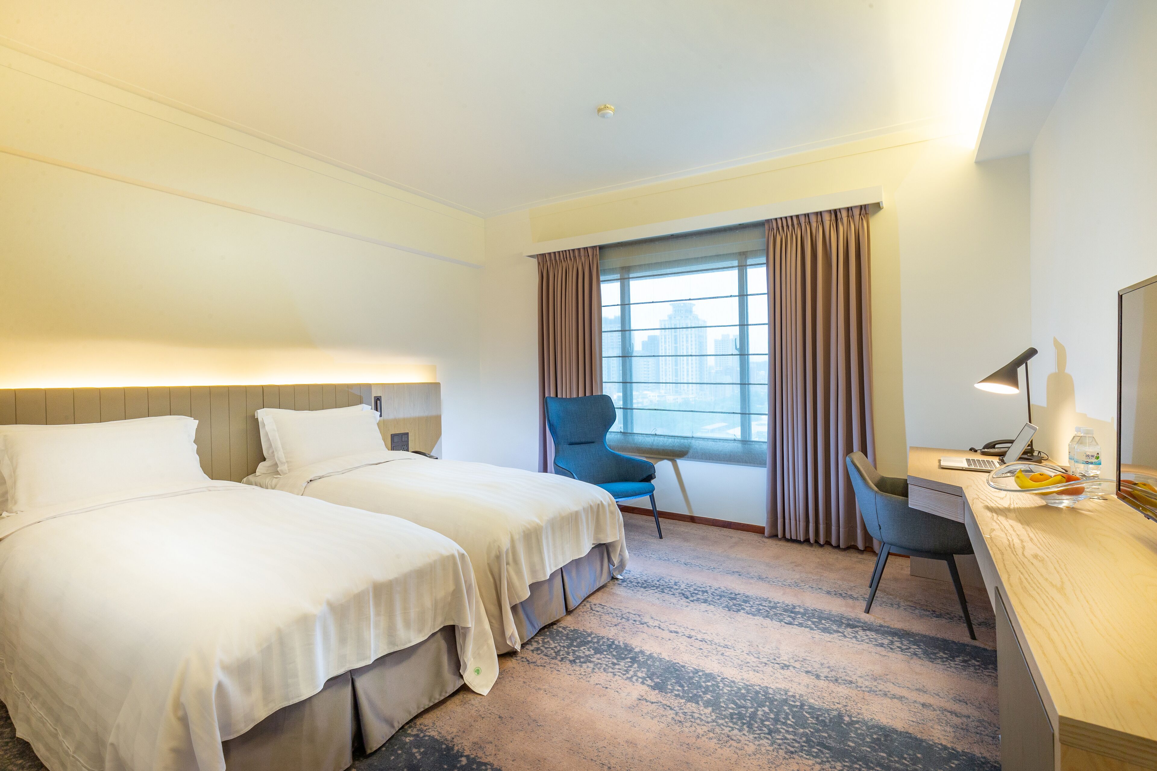 A hotel room with two beds, a desk, a chair, and a window with curtains.