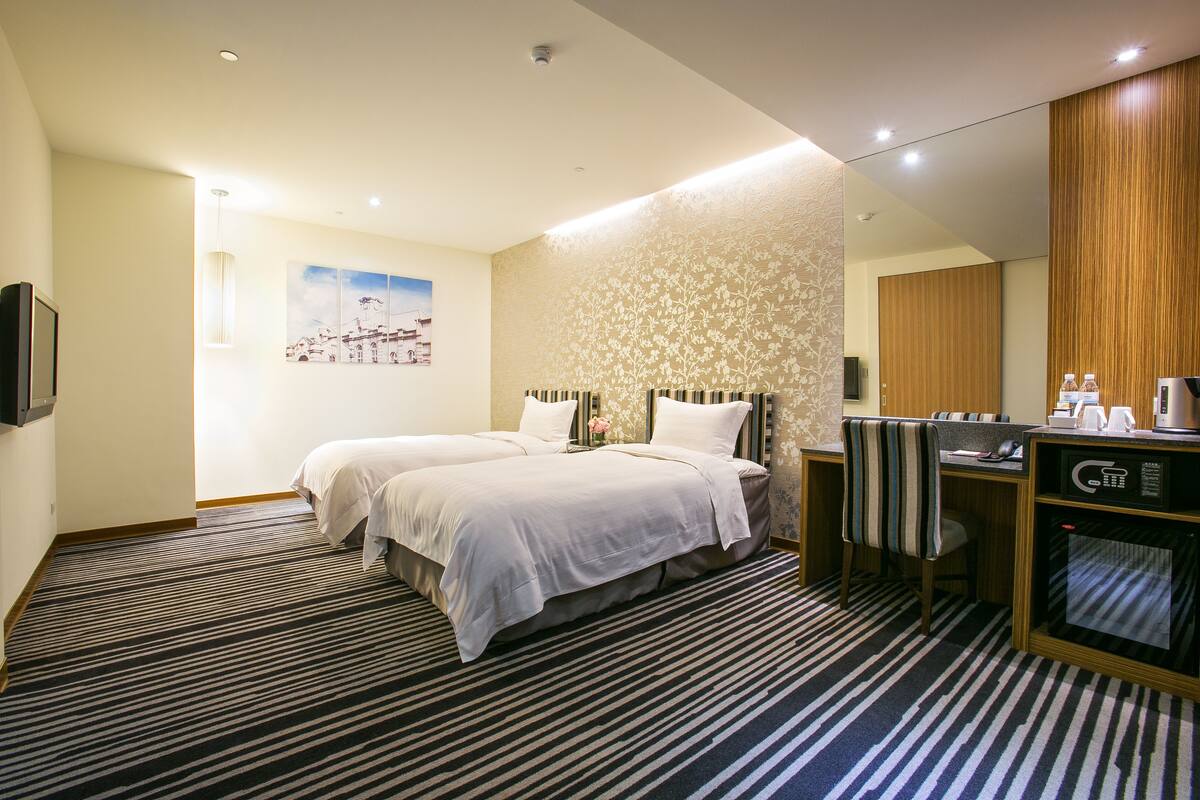 Habitación de hotel con dos camas, un escritorio, un microondas y un espejo grande.