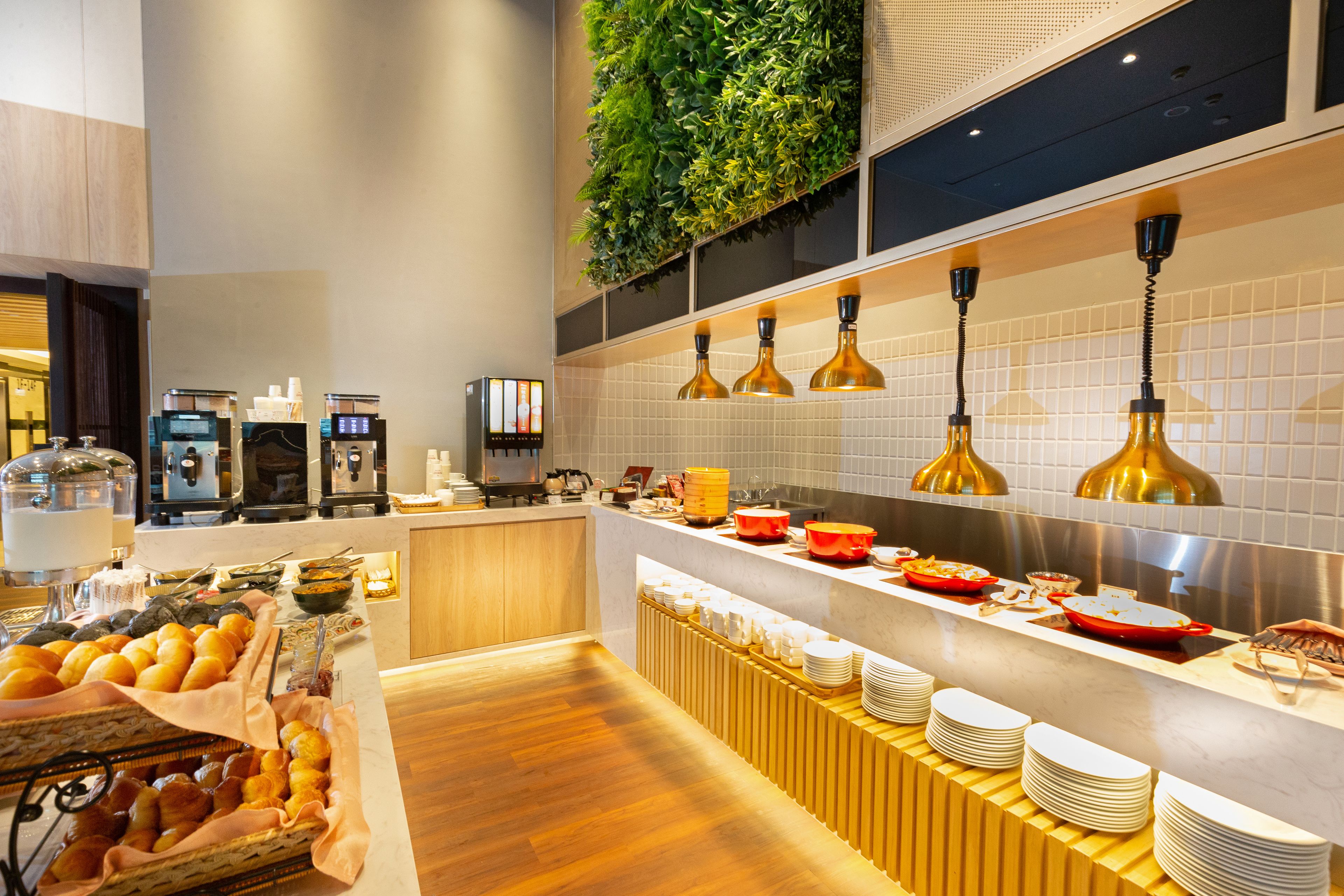 Un buffet de petit-déjeuner moderne proposant une grande variété d’aliments, un espace dédié au café et un mur végétal.