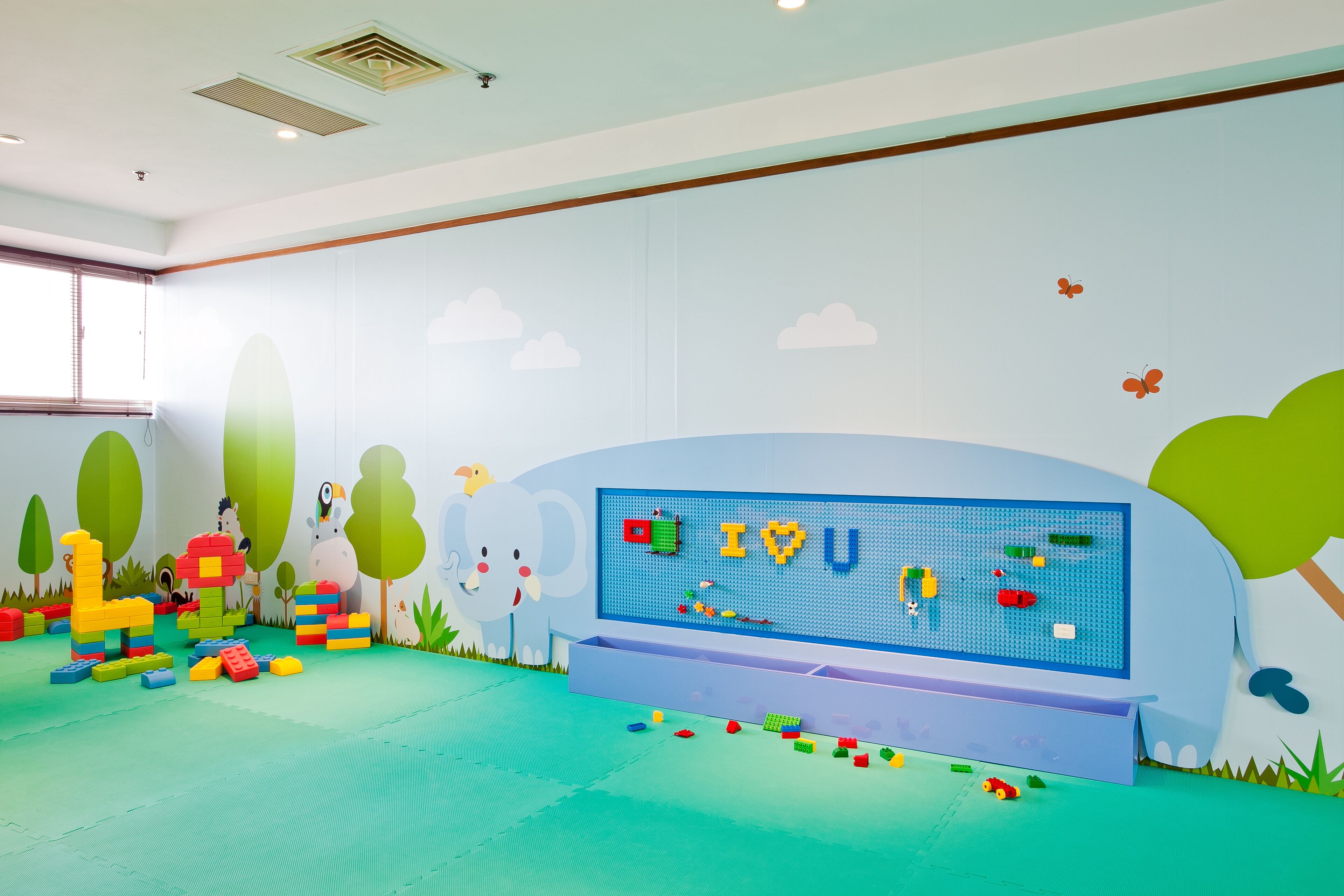 A play area with colorful toys, a large play mat, and a wall with a nature-themed mural.