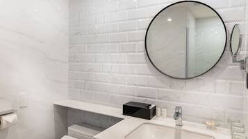A modern bathroom with a white toilet, a black vanity, a round mirror, and a marble-tiled wall.