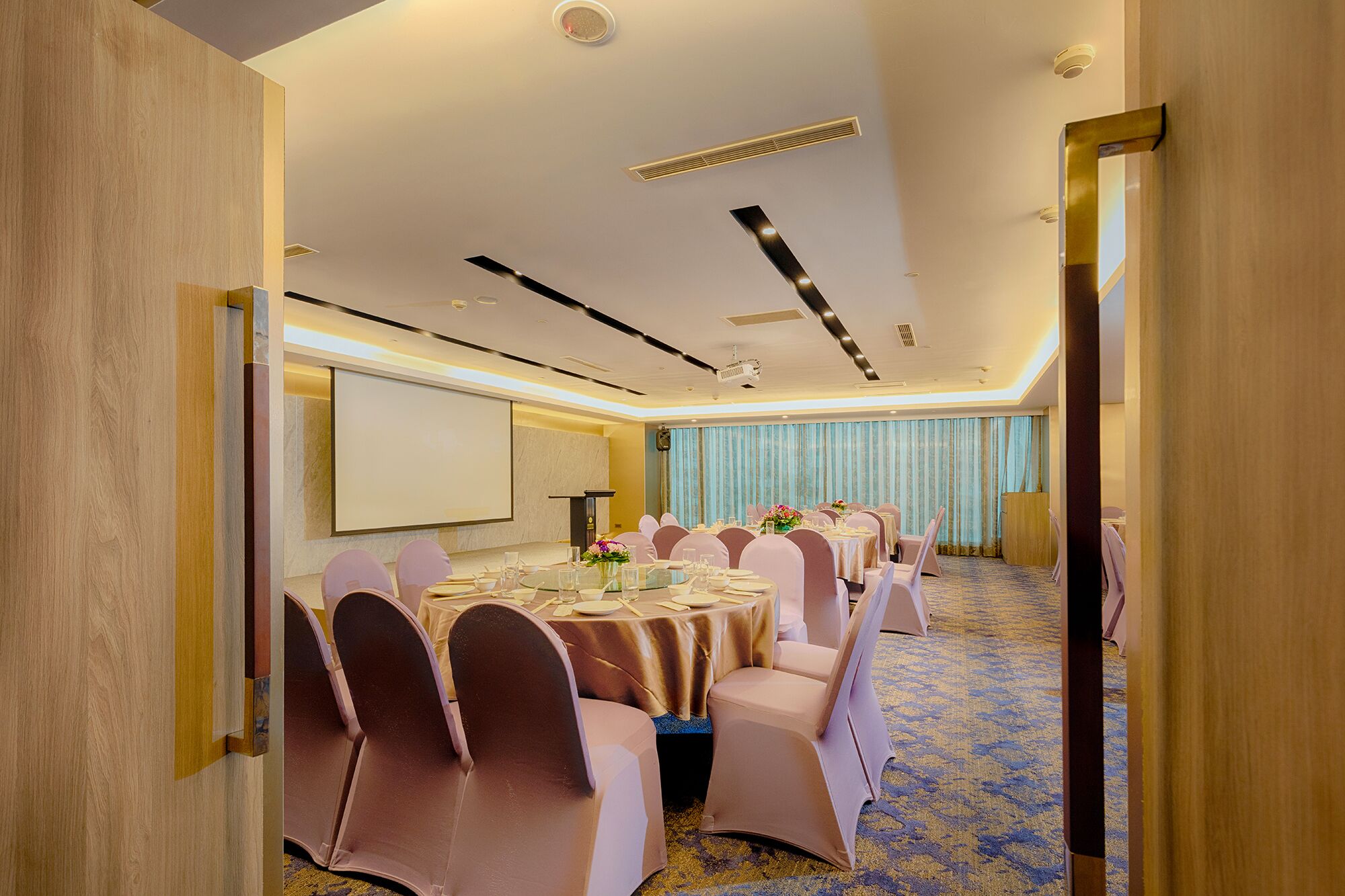 A conference room with round tables, chairs, a projector screen, and a carpeted floor.