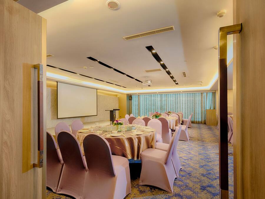 A conference room with round tables, chairs, a projector screen, and a carpeted floor.