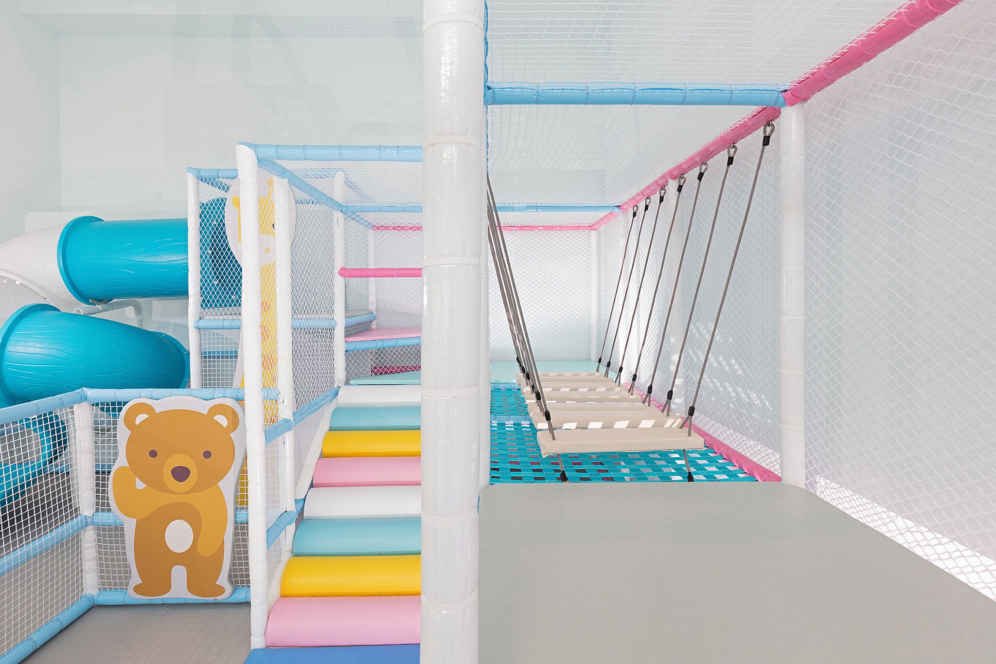 Ein Kinderspielbereich mit einer Rutsche mit Bärenmotiv und Kletterwänden mit Netz.