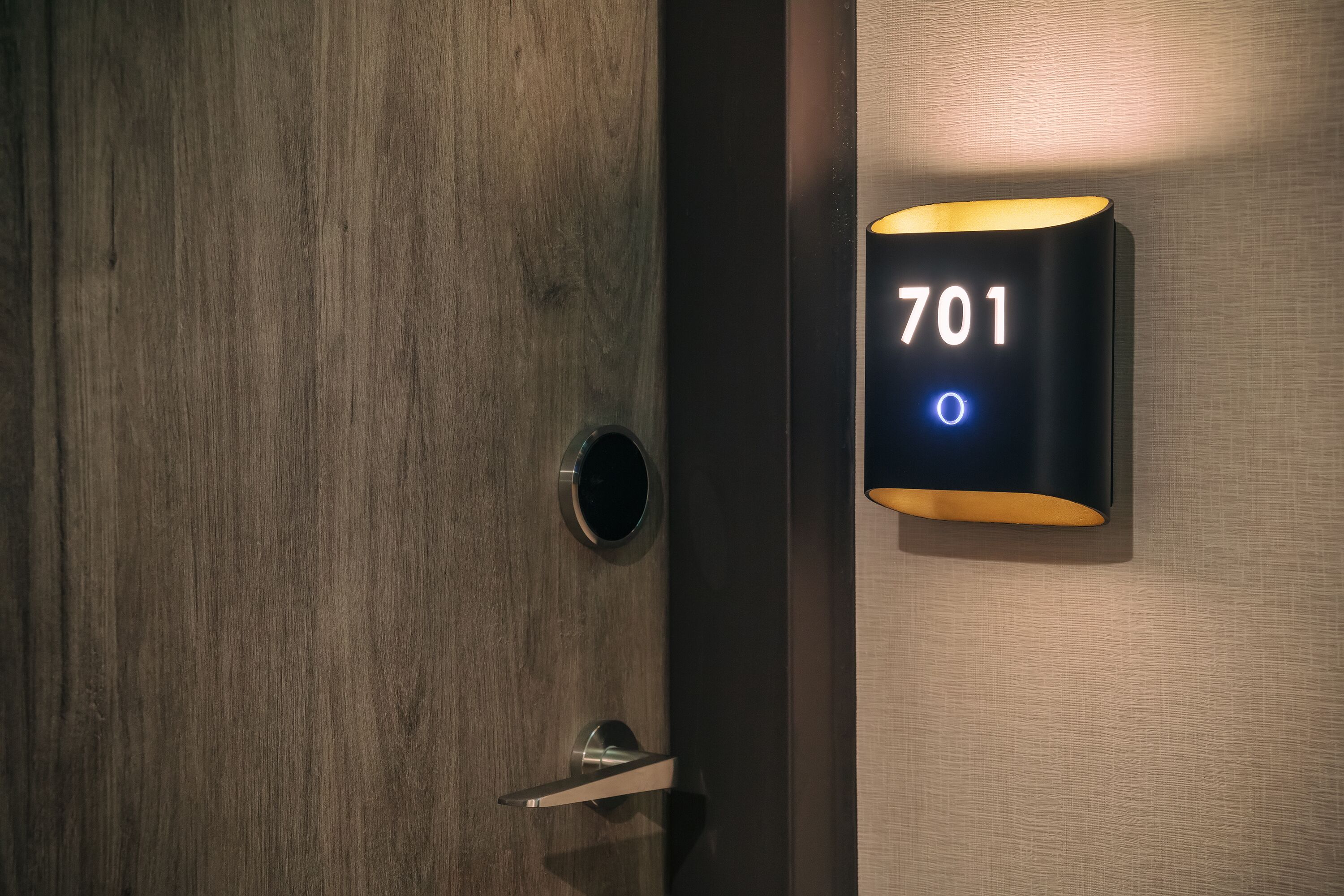Une porte en bois dotée d’un trou de serrure et d’un luminaire moderne affichant le numéro 701.