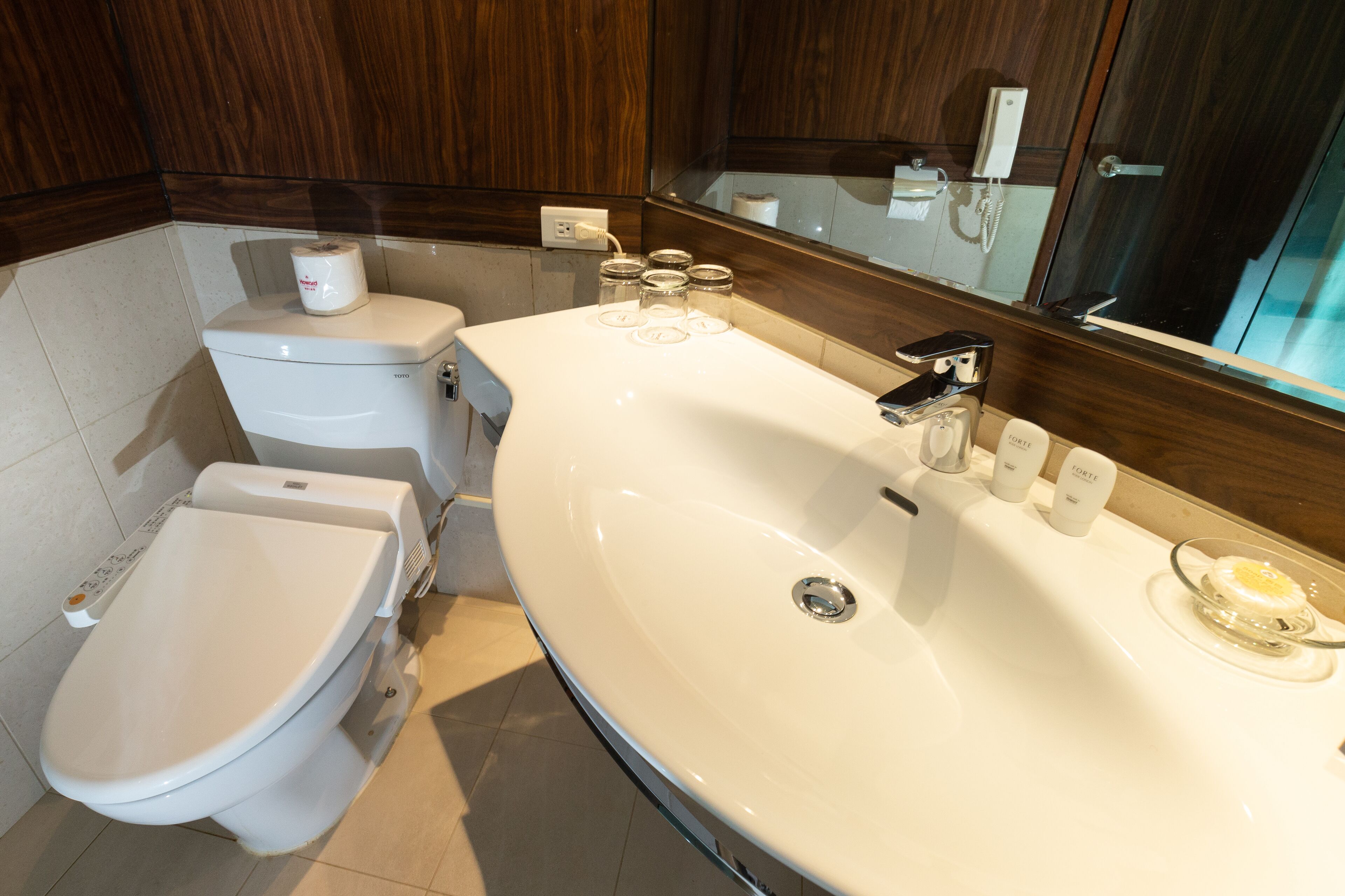 A modern bathroom with a white toilet, a large sink, and a mirror above the sink.