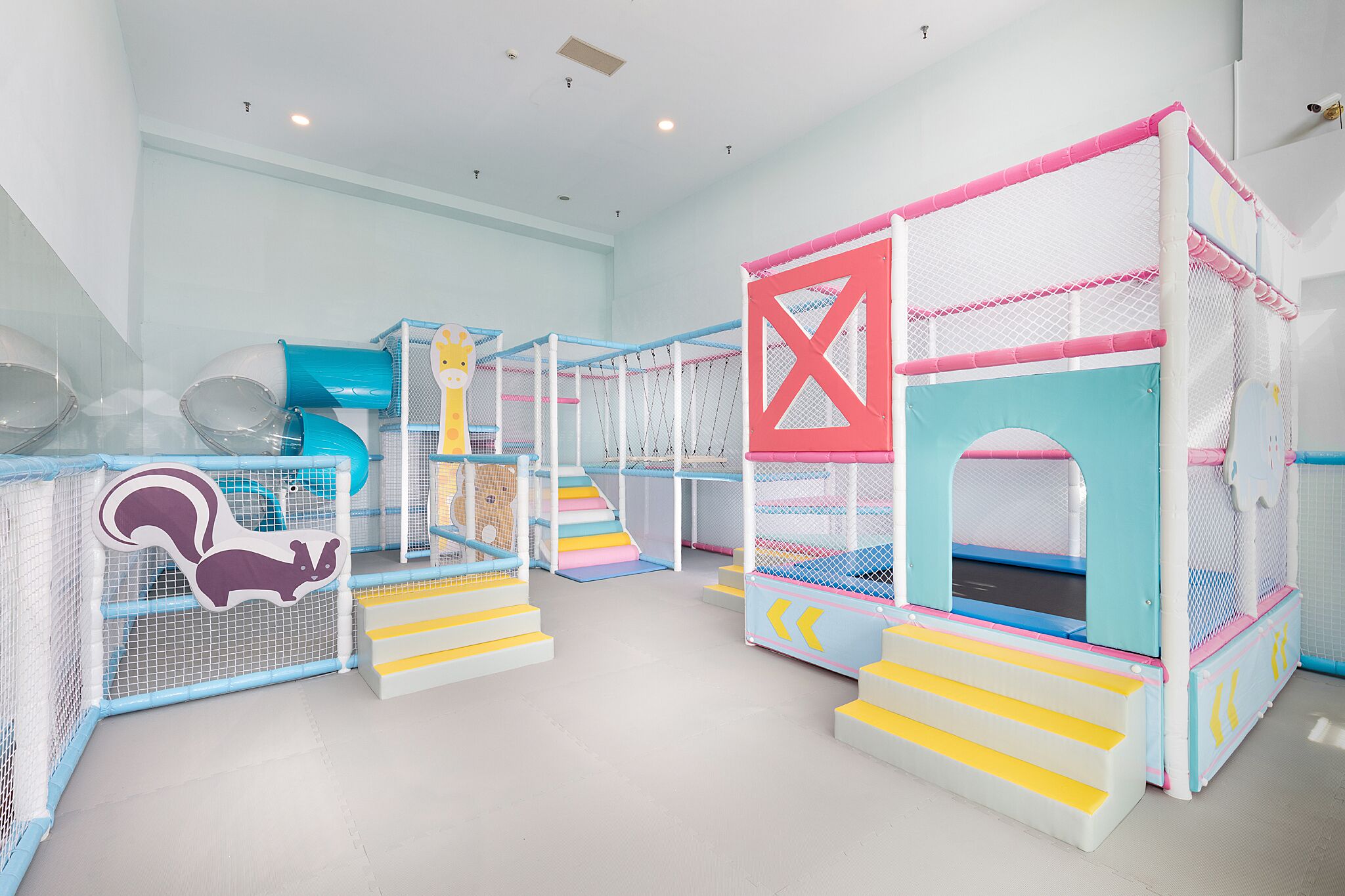 Un área de juegos infantiles con varias estructuras, incluyendo un tobogán, una red de escalada y una casita pequeña cerrada.