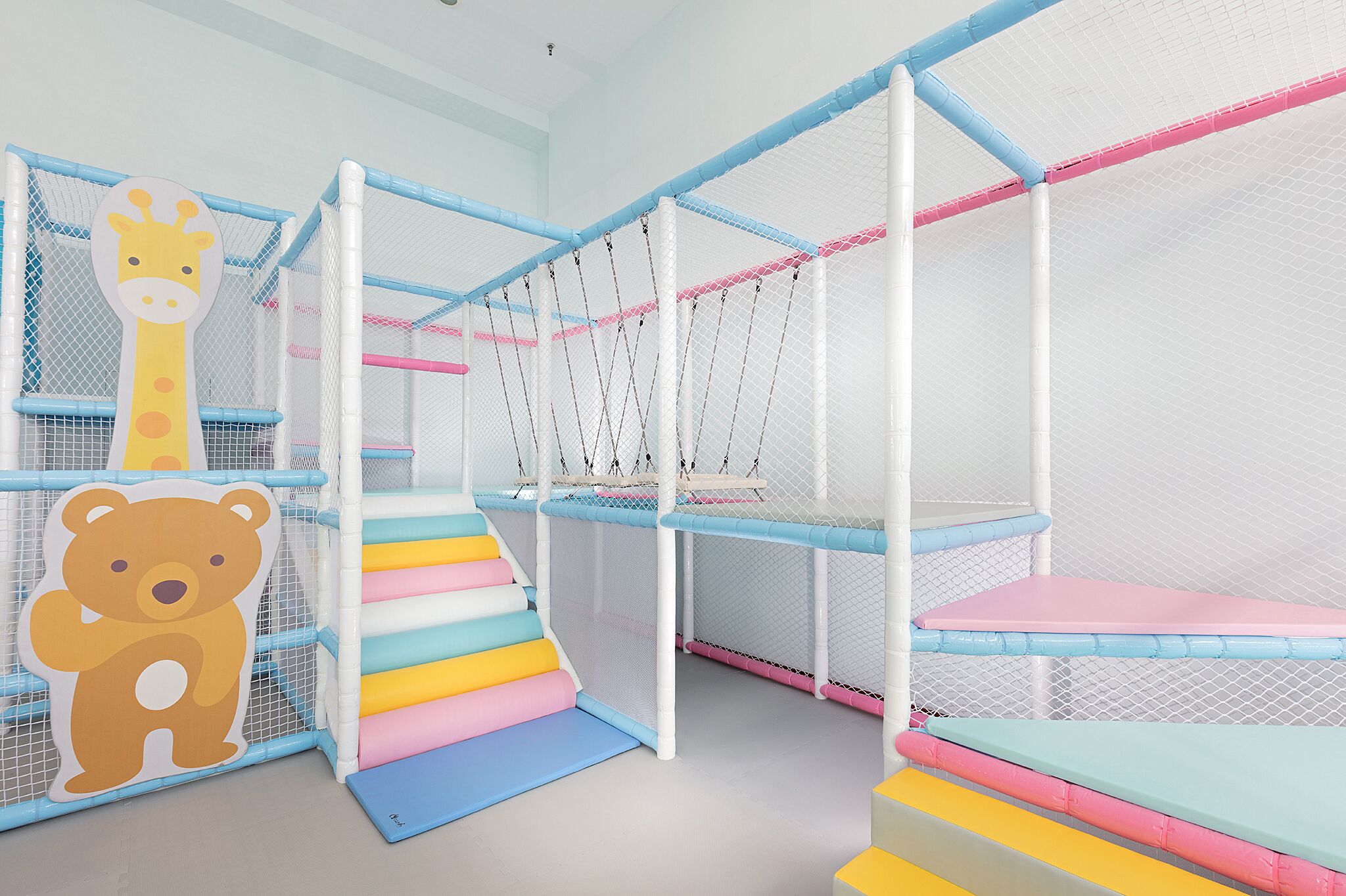 Ein Spielbereich für Kinder mit einer Kletterkonstruktion aus Netzen und bunten Stufen.