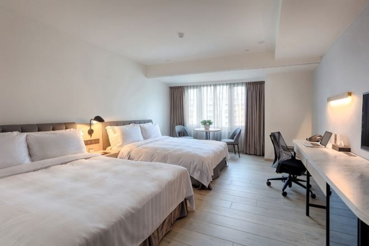 Habitación de hotel con dos camas, un escritorio, una silla y una mesita con una planta.