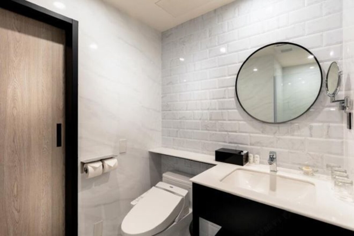 Un baño moderno con inodoro blanco, lavamanos con espejo y dispensador de papel higiénico.