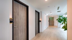 Een moderne hal met houten deuren, een digitaal kamer nummer display en een potplant.