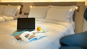 Een net opgemaakt bed met witte lakens, een laptop, een boek, een beker en een appel op het bed.