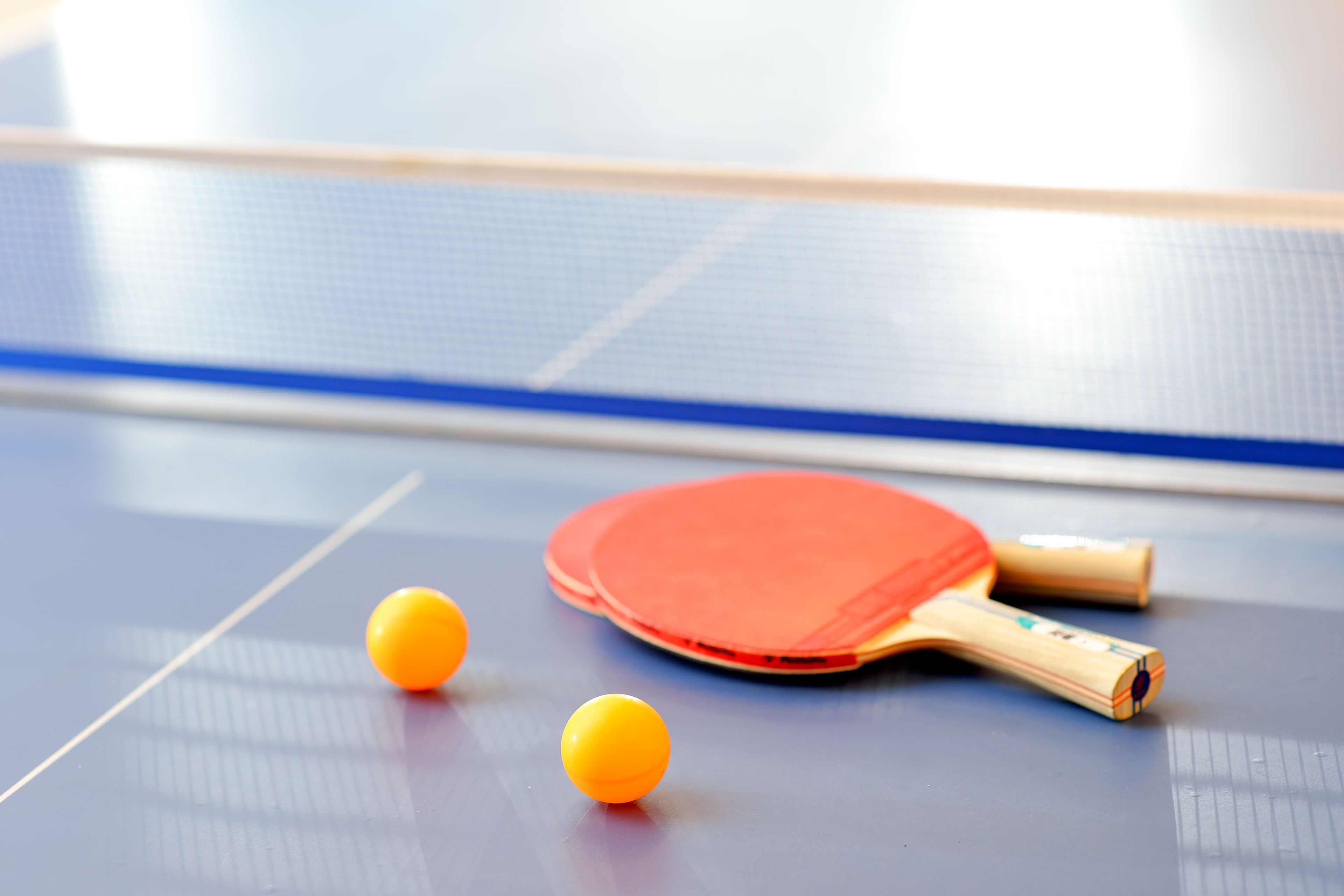A table tennis table with a red paddle and two yellow balls.