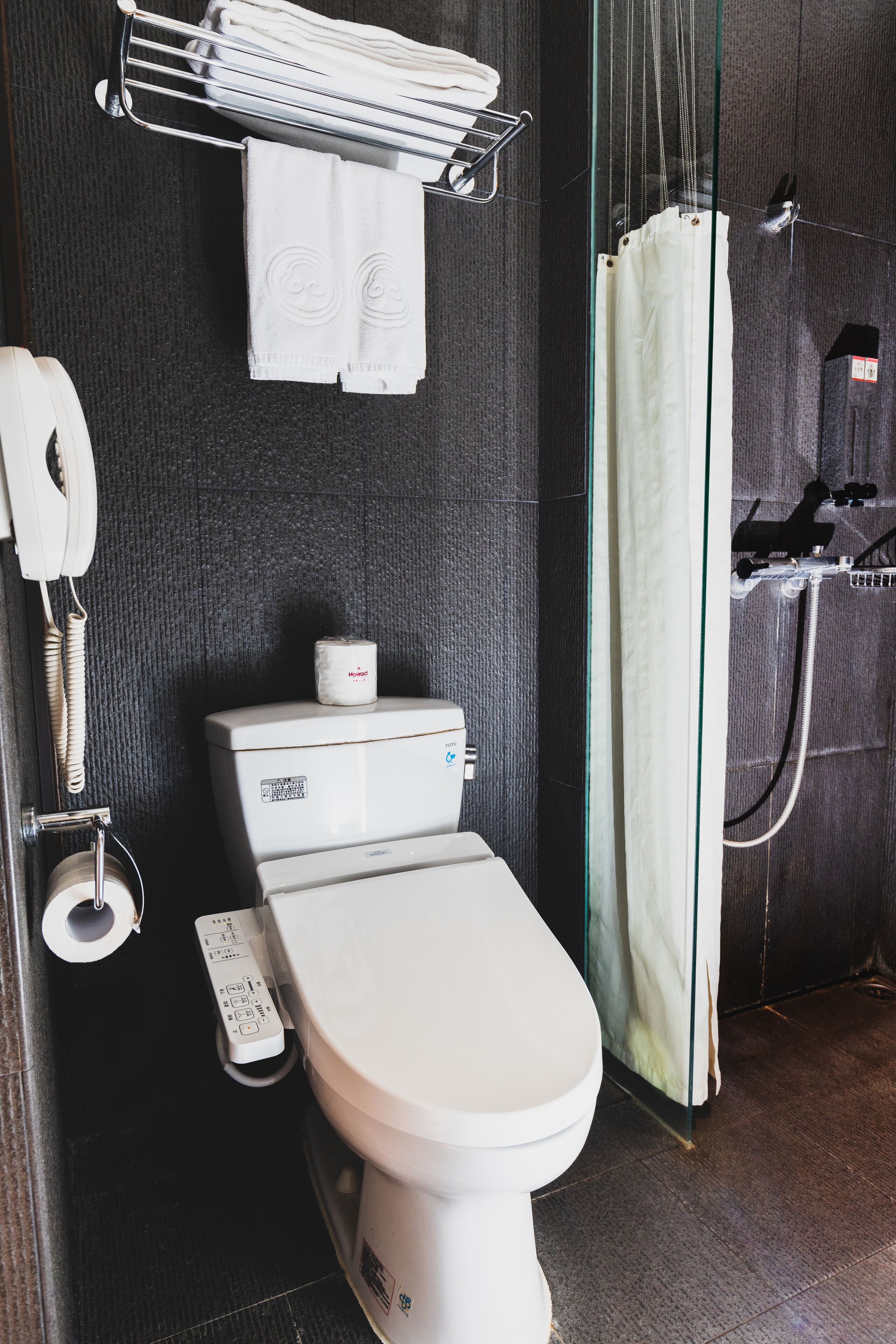 Une salle de bain moderne équipée de toilettes, d’un sèche-mains, d’un porte-serviettes et d’un rideau de douche.