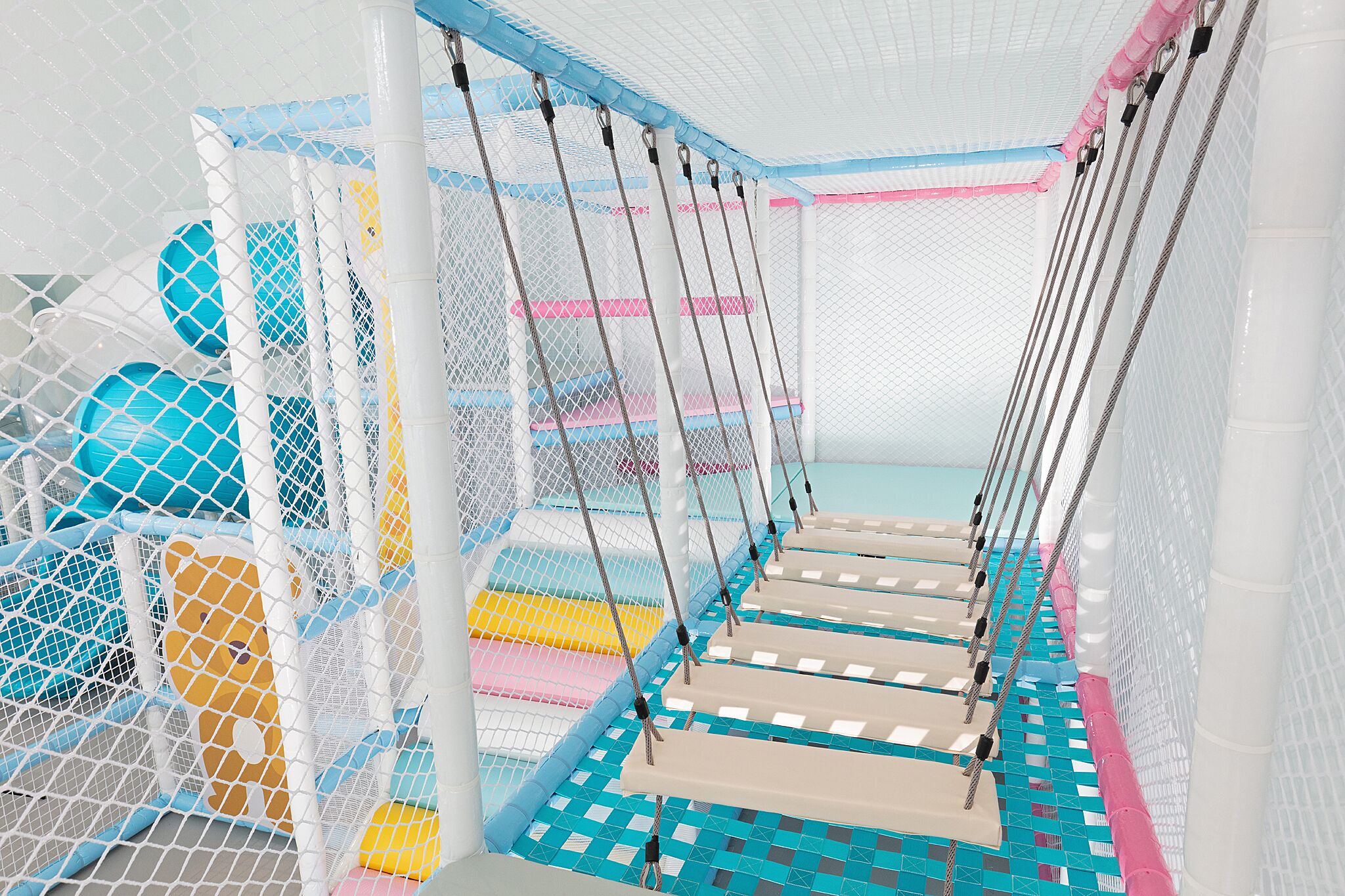 A play area with netted safety zones, padded platforms, and colorful play structures.