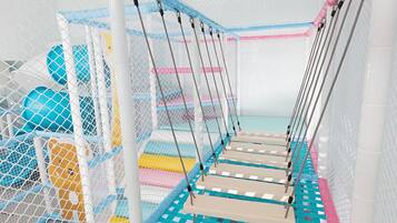 A play area with netted safety zones, padded platforms, and colorful play structures.