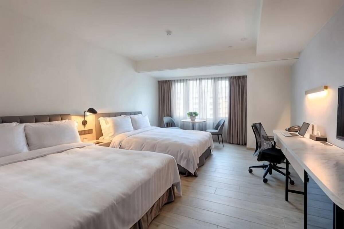 Habitación de hotel con dos camas, un escritorio, una silla y una mesita con una planta.
