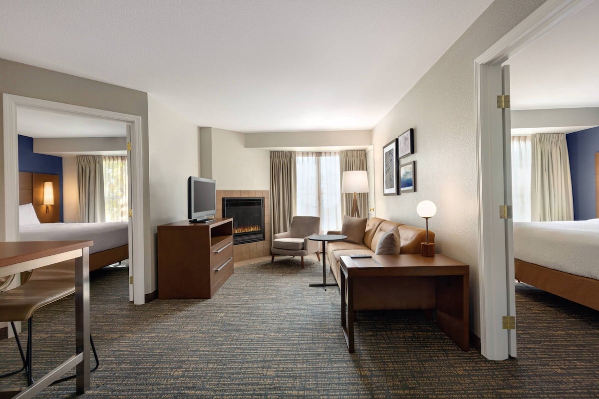 A hotel room with a bed, a desk, a chair, a TV, a fireplace, and a sofa.