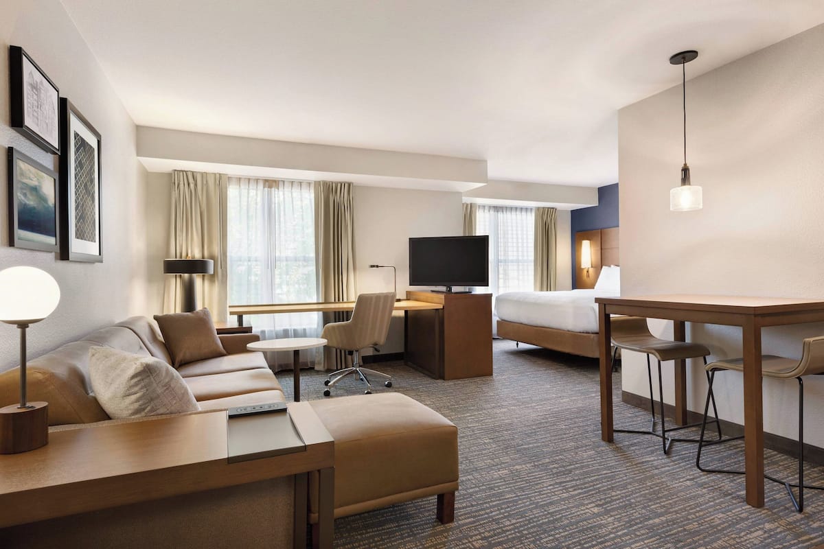 A hotel room with a sofa, a desk, a TV, and a bed.