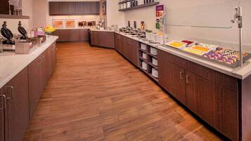 A modern hotel kitchen with wooden flooring, stainless steel appliances, and a buffet area with various food items.