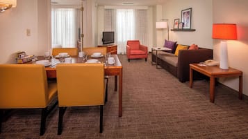 Une chambre d’hôtel comprenant un coin repas, un canapé, une télévision et une lampe.