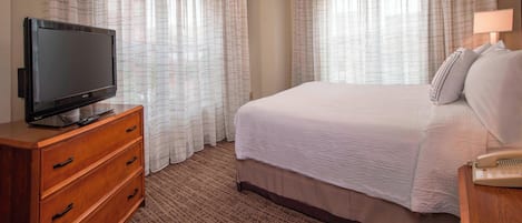 A hotel room with a large bed, a wooden dresser with a flat-screen TV, and a bedside table with a lamp.