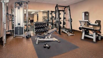 Ein Fitnessstudio mit verschiedenen Trainingsgeräten, darunter Kurzhanteln, eine Bank und Kraftgeräte.